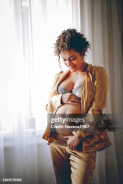 sensual pregnant woman standing beside the window at hom - hom stock pictures, royalty-free photos & images