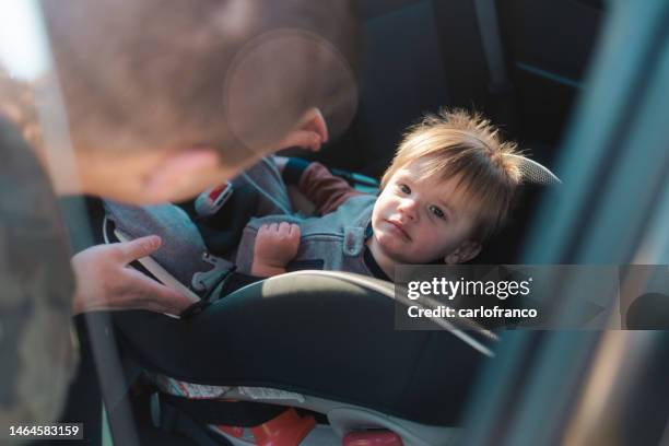 autositz - papa schnallt seinen sohn für eine fahrt an - military family baby stock-fotos und bilder