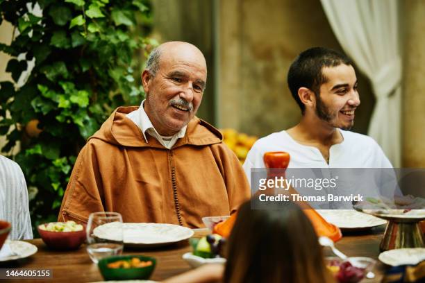 smiling mature uncle in discussion during family celebration dinner - arab old man fotografías e imágenes de stock
