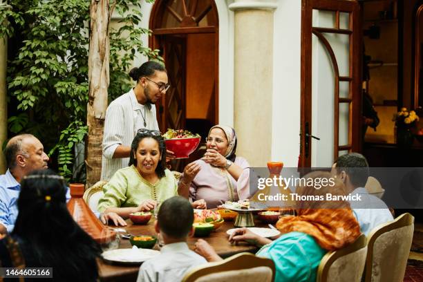 wide shot of nephew bringing salad to table during family dinner - arab family eating fotografías e imágenes de stock