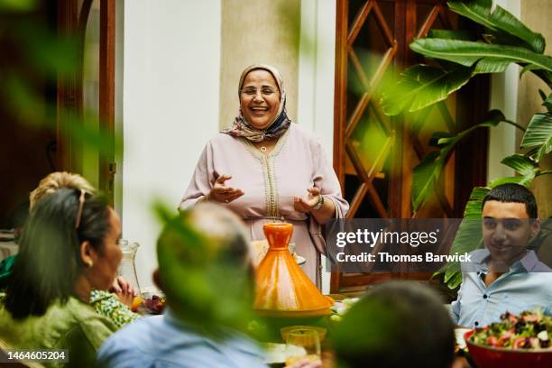 medium shot of smiling mature woman giving toast during family dinner - islam family stock pictures, royalty-free photos & images