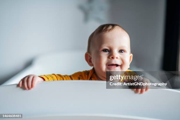 charming baby boy looking through his crib. - alleen één jongensbaby stockfoto's en -beelden