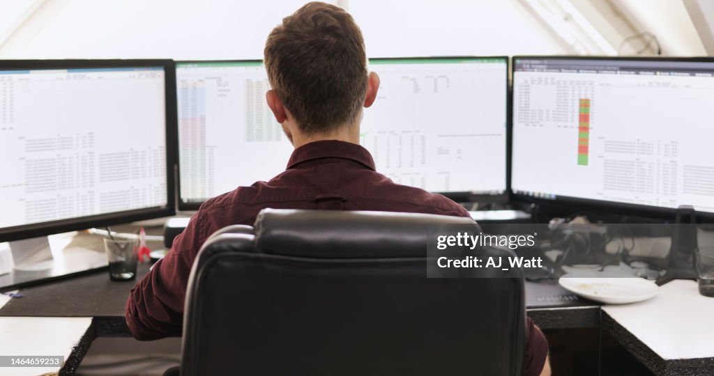 Young businessman working on multiple computer monitors at his desk