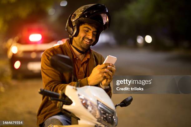 happy man chatting on mobile phone while sitting on motorcycle at night - indian city roads stock pictures, royalty-free photos & images