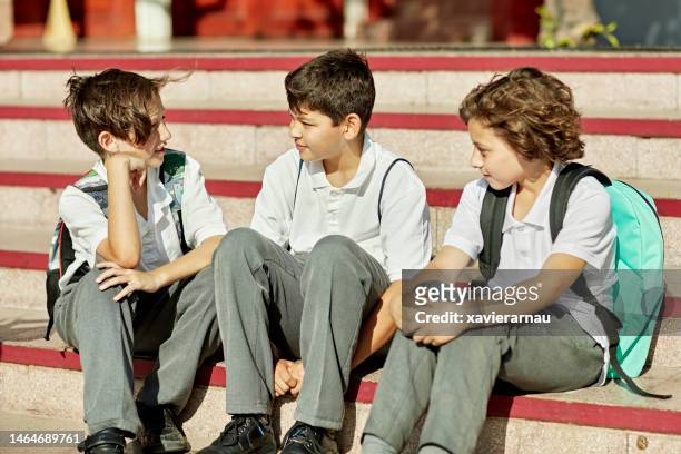 pre-adolescent schoolboys sitting outdoors and talking - alleen jongens stockfoto's en -beelden