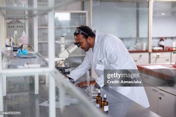 side view of an african male scientist analyzing a sample through a microscope at a lab - scientist standing next to table stock pictures, royalty-free photos & images