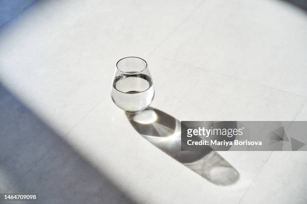 a glass of water stands on a white marble floor in the rays of the bright sun. - drinking glass of water stock pictures, royalty-free photos & images