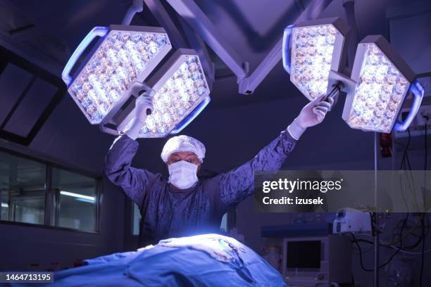 male nurse adjusting lights over patient in operating theater at hospital - surgical mask and gloves stock pictures, royalty-free photos & images