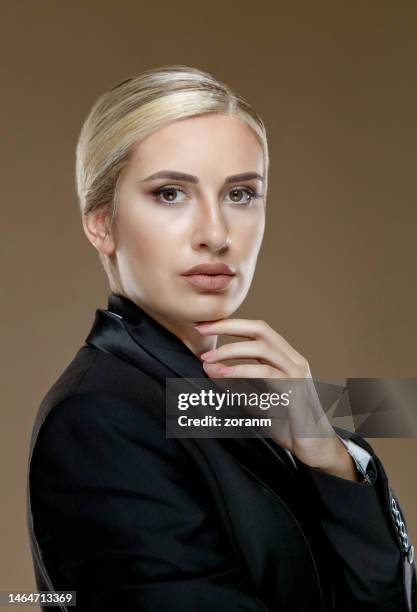 portrait of beautiful young woman with blond hair back, wearing black jacket and looking at camera - blonde hair brown eyes stock pictures, royalty-free photos & images