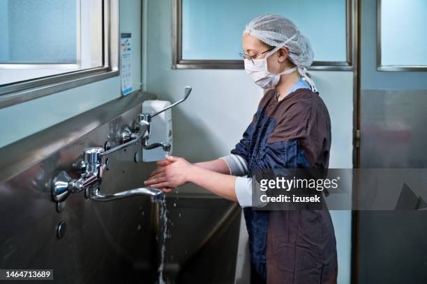 side view of female surgeon washing hands under faucet in sink at hospital - schoonschrobben stockfoto's en -beelden