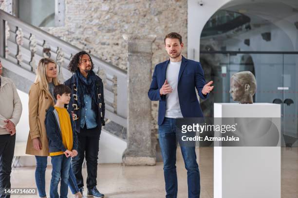 erwachsener kaukasischer männlicher museumsführer, der einer vielfältigen gruppe von menschen eine tour durch das museum gibt - guide stock-fotos und bilder