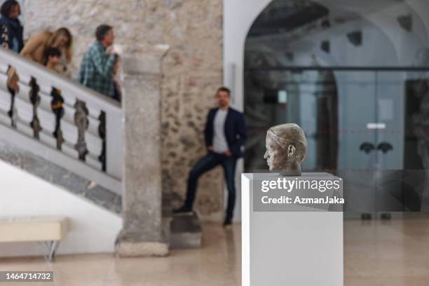 statue eines männerkopfes in einem museum mit museumsführer und besuchern im hintergrund - museumswärter stock-fotos und bilder