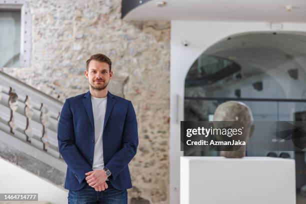 atractivo guía turístico masculino caucásico adulto mirando a la cámara mientras está de pie junto a una estatua de la cabeza de un hombre en un museo - curator fotografías e imágenes de stock