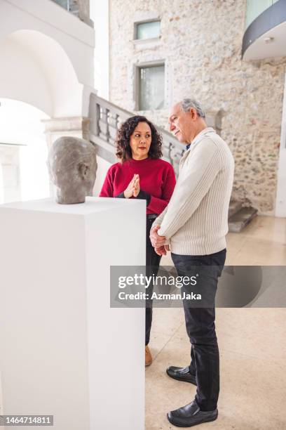 ernsthafte erwachsene frau, die ihren älteren kaukasischen ehemann ansieht, während er die statue in einem museum betrachtet - bust museum stock-fotos und bilder