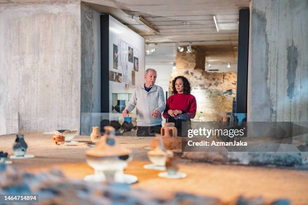 passionate senior caucasian male explaining the importance of history to his wife while they are looking at the history exhibition in a museum - gallery 2 stock pictures, royalty-free photos & images