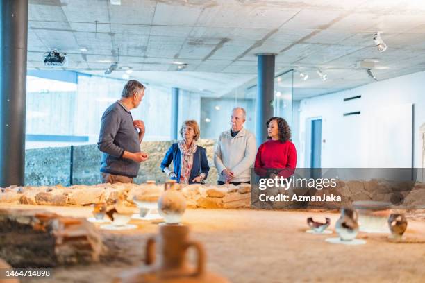 a senior caucasian museum employee giving a museum tour to a group of senior museum visitors - museum guide stock pictures, royalty-free photos & images