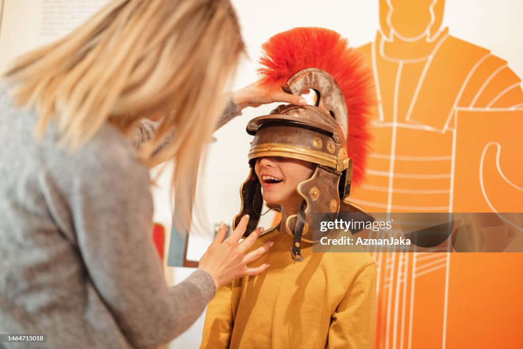 Blonde kaukasische Mutter legt Roman Galea auf den Kopf ihres glücklichen kleinen Sohnes, während sie ein Museum besuchen