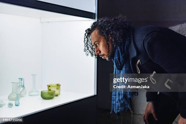 interested adult black male looking at a showcase of glassware in a history museum - cristaleira imagens e fotografias de stock