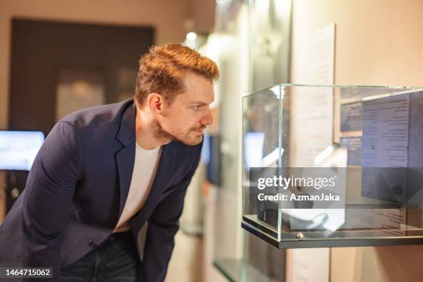 adult caucasian male museum visitor looking at a small statue in display case in a history museum - history museum stock pictures, royalty-free photos & images