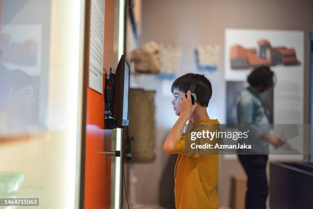 caucasian young boy putting on headphones to listen to an audio guide in a museum - history museum stock pictures, royalty-free photos & images