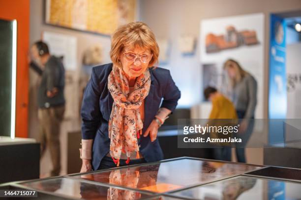 smart senior kaukasische frau, die ein museum besucht und von den historischen funden fasziniert ist - museum besucher stock-fotos und bilder