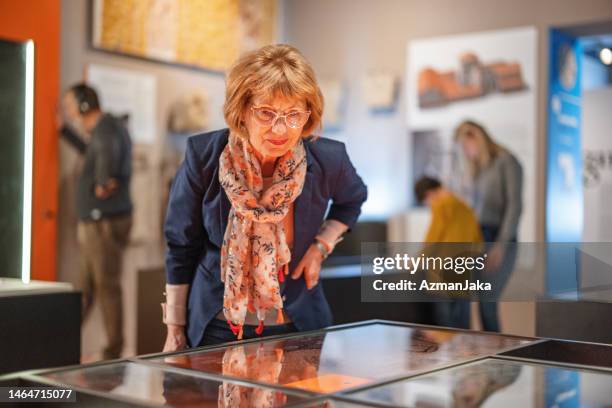 mujer caucásica mayor inteligente visitando un museo y fascinada por los hallazgos históricos - expo 70 fotografías e imágenes de stock