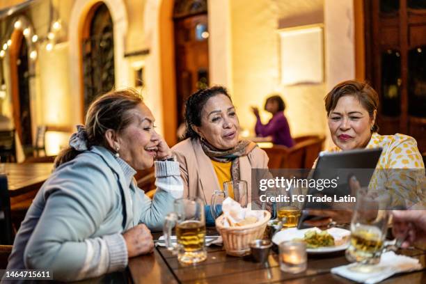 senior friends having fun while using digital tablet at restaurant - online happy hour stock pictures, royalty-free photos & images