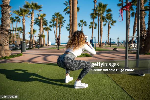 young blonde woman with long curly hair doing back squats in park - female backside stock pictures, royalty-free photos & images