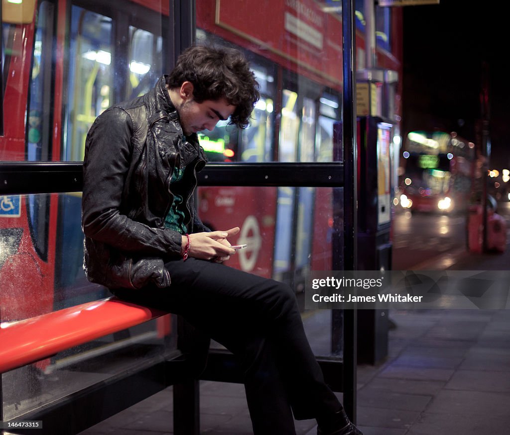 Young man checks phone at bus stop