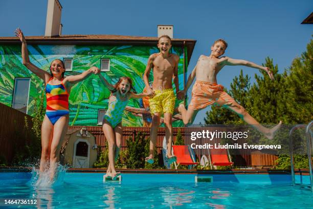 four cute teen kids in swim suits jumping together into the pool at back yard. - family playing in backyard pool stock-fotos und bilder