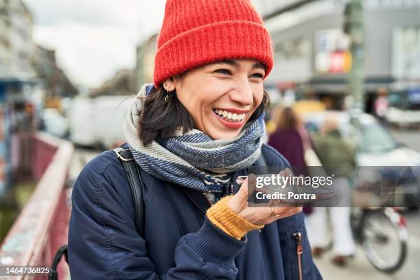 cheerful young woman talking on speaker phone outdoors in city - conference phone stock pictures, royalty-free photos & images