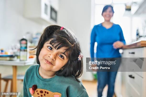 cute little girl with mother at back in kitchen - hoofd schuin stockfoto's en -beelden
