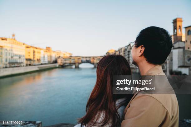 ein asiatisches paar umarmt sich auf der santa trinita brücke mit ponte vecchio im hintergrund - florenz, italien - vecchio stock-fotos und bilder