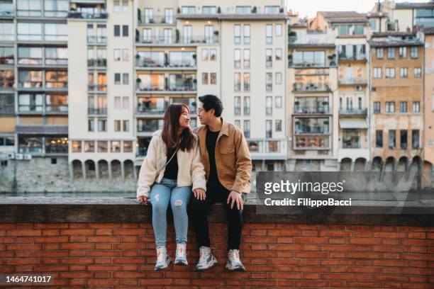 An asian couple is sitting on Lungarno in Florence, Italy