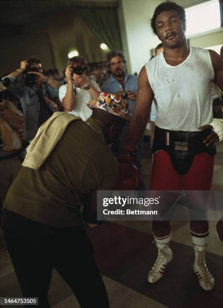 Heavyweight champion George Foreman has his boxing glove removed by trainer Dick Sadler, after a workout before the title bout in Kinshasa, Zaire, on...