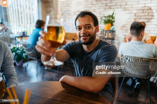 portrait of a young man drinking beer in a bar - man sipping beer smiling stockfoto's en -beelden