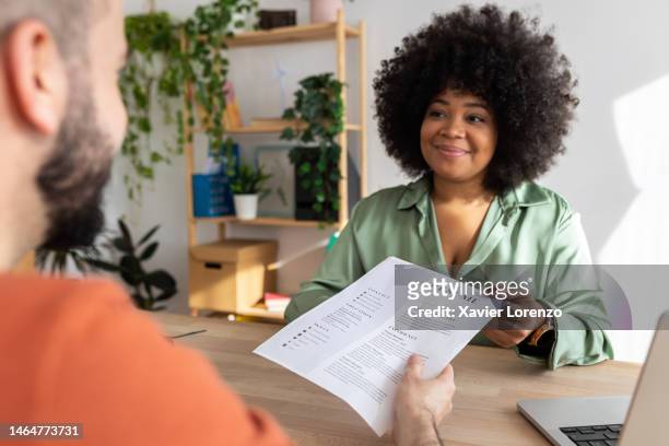 young adult caucasian male job candidate giving resume to latin american female hr recruiter manager at work interview. human resources, business recruitment and job interview concept - colloquio di lavoro foto e immagini stock