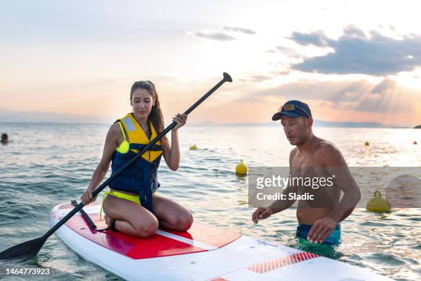 teenage girl learning how to paddle boarding with instructor - paddleboarding team stock pictures, royalty-free photos & images