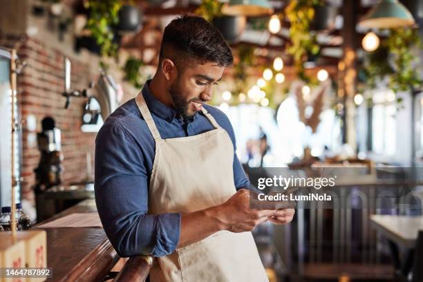cafe, small business and man texting or reading, social media and blog review. businessman, startup and indian entrepreneur chatting, online or using app in a coffee shop, content and satisfied - small restaurant stock pictures, royalty-free photos & images