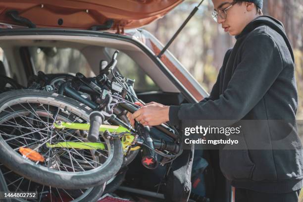 kleiner teenager nimmt sein ordnerfahrrad aus dem kofferraum eines autos - zusammenklappbar stock-fotos und bilder