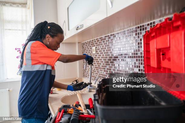 fontanera negra arreglando una fuga en el fregadero de la cocina de una casa - spoil system fotografías e imágenes de stock