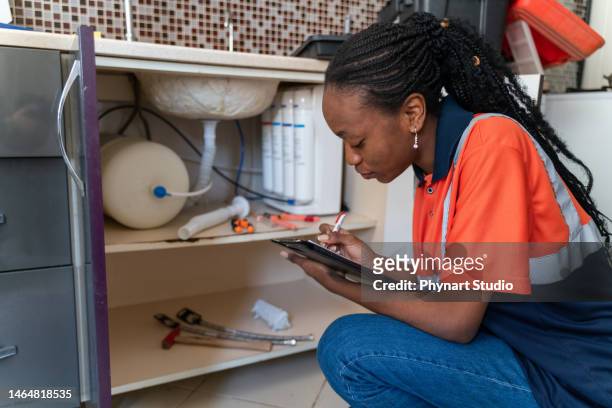 black female plumbing technician checking water installation with notepadb - kitchen straighten stock pictures, royalty-free photos & images