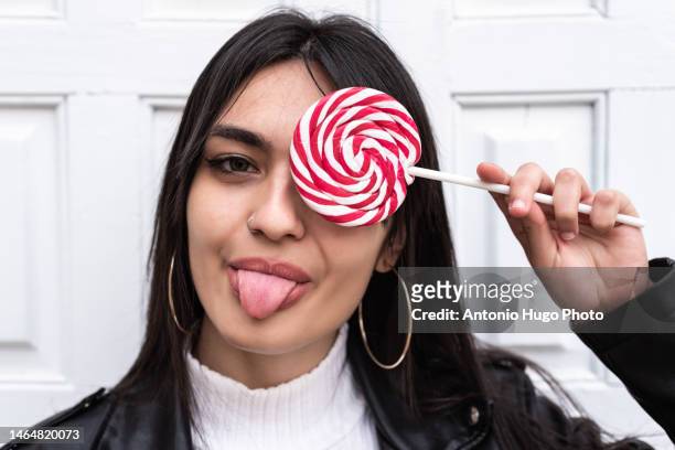 portrait of spanish brunette girl covering one eye with a colorful lollipop - candy on tongue stock pictures, royalty-free photos & images