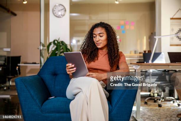 young businesswoman tablet computer while sitting on armchair at office - tablet benutzen stock-fotos und bilder