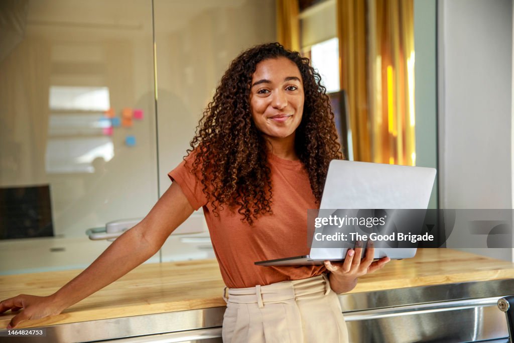 Smiling female entrepreneur with laptop standing in office
