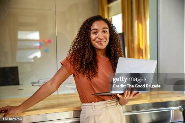 smiling female entrepreneur with laptop standing in office - smart casual laptop stock pictures, royalty-free photos & images