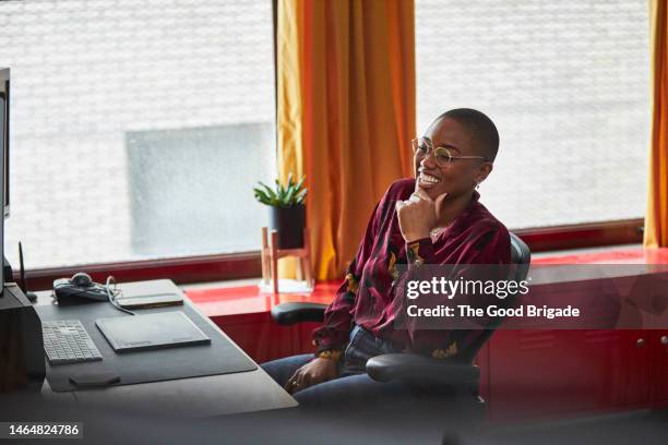 cheerful businesswoman with hand on chin sitting in office - red blouse stock pictures, royalty-free photos & images