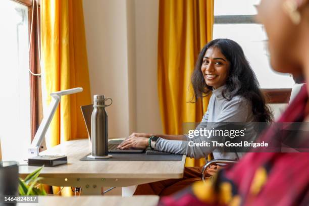 smiling businesswoman with laptop looking at colleague while sitting in office - reusable water bottle office stock pictures, royalty-free photos & images