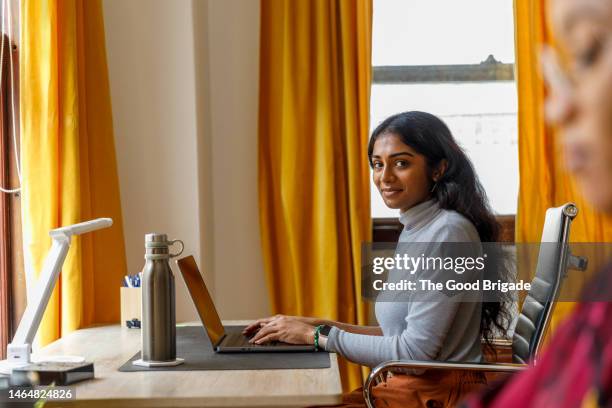 portrait of smiling young female entrepreneur sitting at desk in office - reusable water bottle office stock pictures, royalty-free photos & images