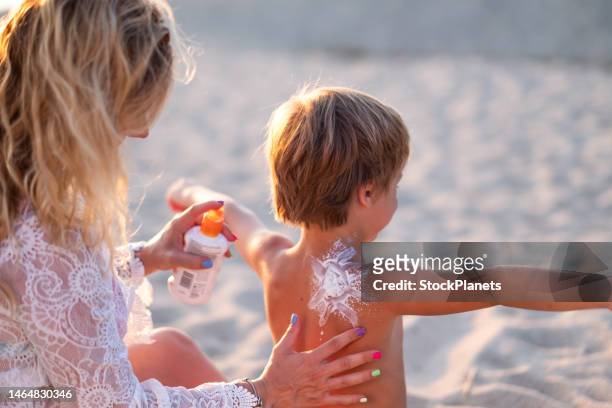 eine mutter trägt sonnencreme auf den rücken ihres kindes am strand auf. - sunburn tourist stock-fotos und bilder